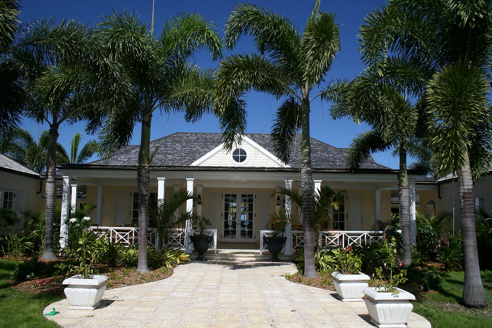 A Jumby Bay residence — formal entrance with royal palms, classical colonnade and cedar-shake hipped roof. Built by Elderfield Gibbs Smith, Master Builder.